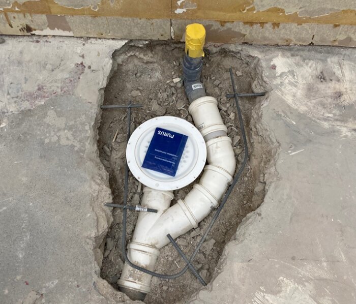 Installation av Purus NOOD vattenlås i en golvbrunn med rörkopplingar, i ett pågående byggprojekt.