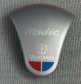 Ny Vårgårda Nordic plastdetalj i grått med logotyp och blå-röd emblem, tillverkad till 1996.