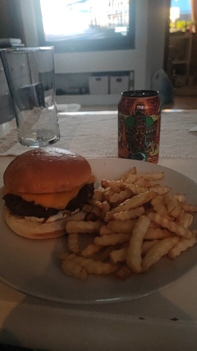 Hamburgare med ost och pommes frites på tallrik framför TV och dryckesburk.