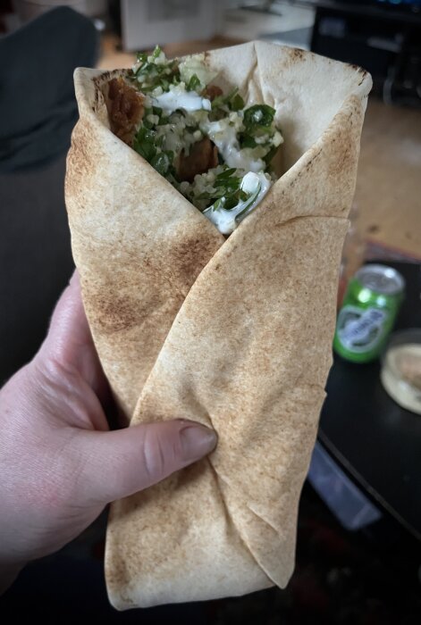 Hand håller en wrap med kyckling, tabbouleh, vitlökssås och hummus i libabröd.