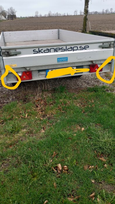Släpvagn parkerad på gräs med två markerade platser på bakänden och en reflex i gult cirklade.