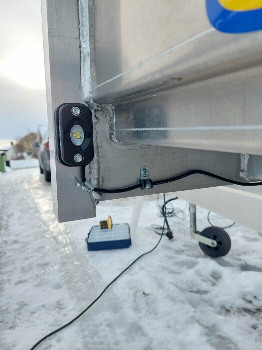 Arbetsljus monterat på släpvagnens kant med kablar och förskruvningar, visar upp installation i vinterscen.