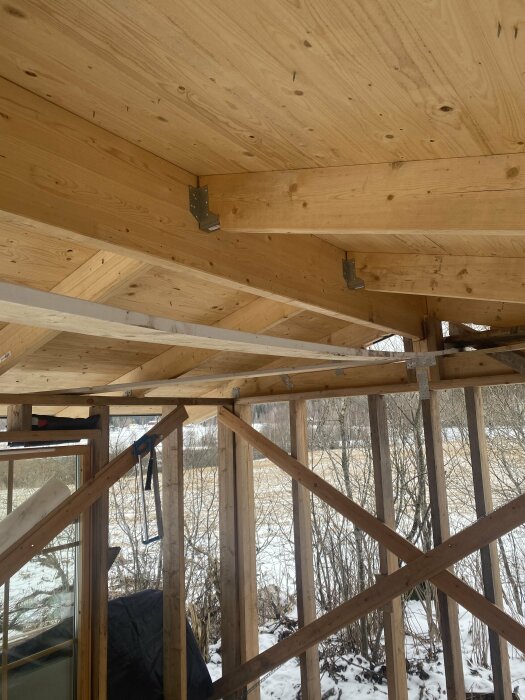 Utsikt från insidan av en lekstuga under konstruktion med synliga träbjälkar och oventilerad taknock.