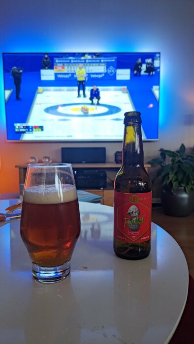 Ölglas och flaska på bord framför TV som visar en curlingmatch.