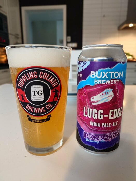 Ett glas öl med Toppling Goliath logotyp bredvid en ölburk från Buxton Brewery på ett köksbänk.