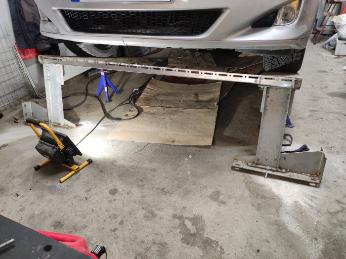 En bil parkerad på metallramper i ett garage för inspektion utan synliga läckage.
