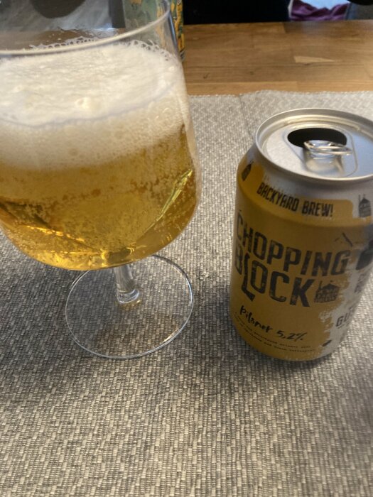 Ölglas fyllt med skummande öl bredvid en ölburk på ett bord, förberedelse inför whiskymässa.