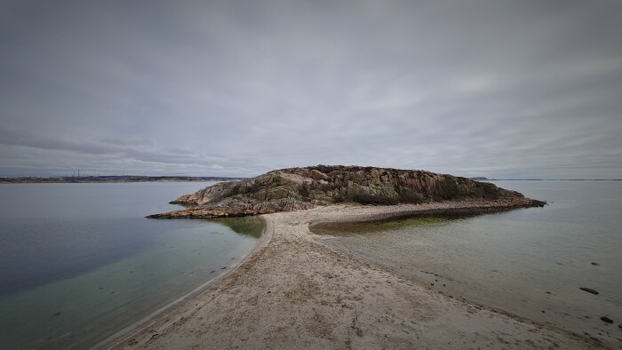 Klippig ö med sandbank i Bohuslän, Sverige, under molnig himmel.