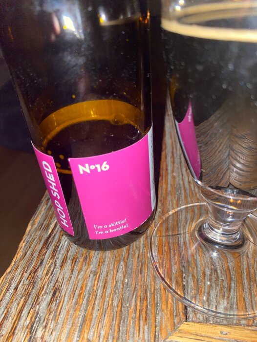 Flaska och glas med Gotlandsbrygd stout på träbord, etikett synlig med texten "No 6 HOP SHED I'm a skittle! I'm a beetle!