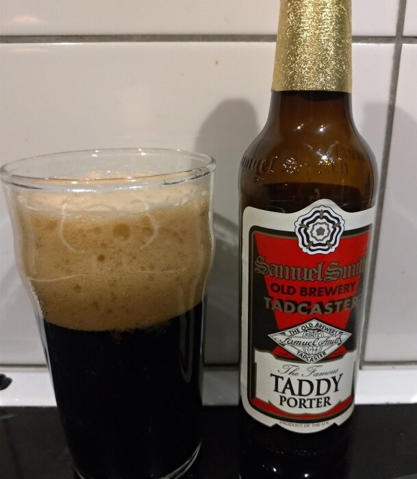 En flaska Samuel Smith's Taddy Porter bredvid ett glas med mörk öl och skum på toppen.