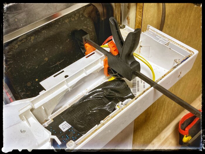 En snabbtving håller fast en knappsats i en diskmaskin under reparation.