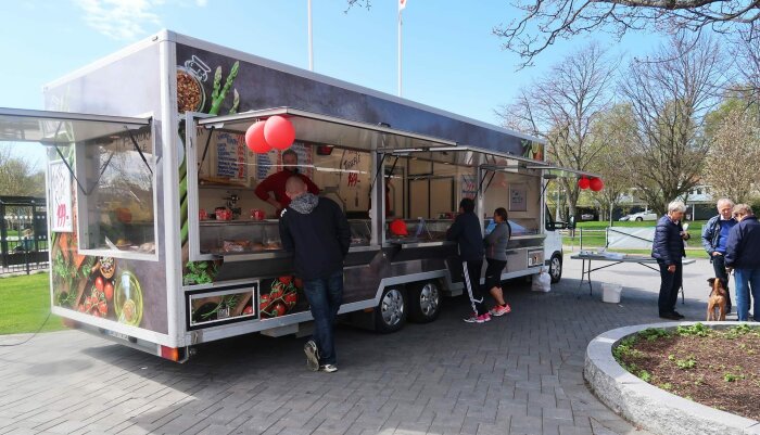 Mobil matvagn med kunder i parkmiljö under dagen.