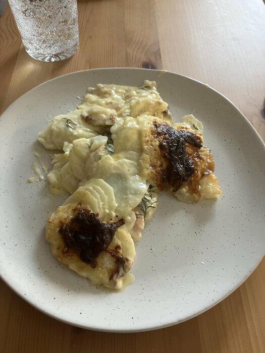 Serverad potatisgratäng med rökt lax på en tallrik, bredvid ett glas med bubbelvatten.