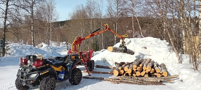ATV med monterad kran som lyfter timmer i ett snöigt landskap.