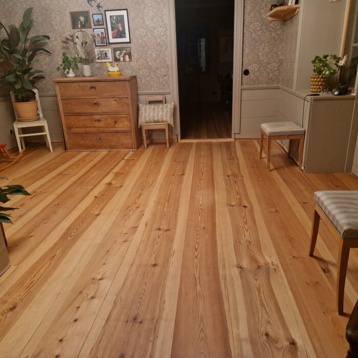 Ett nylagt trägolv i ett vardagsrum med möbler och tavlor, ger ett rent och städat intryck.