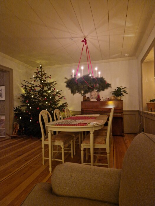 Inredning med julgran och hängande adventsljusstake i ett rum med nylagda trägolv.
