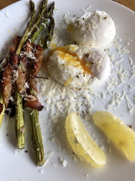 Frukosttallrik med pocherade ägg, baconlindad sparris, riven ost och citronklyftor.