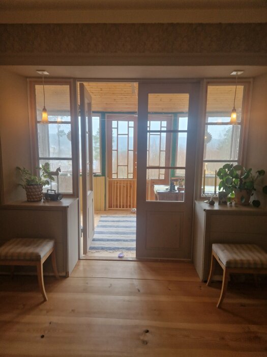 Ett välbelyst rum med trägolv, öppna dubbeldörrar till en veranda, bänkar och en hängande lamp.