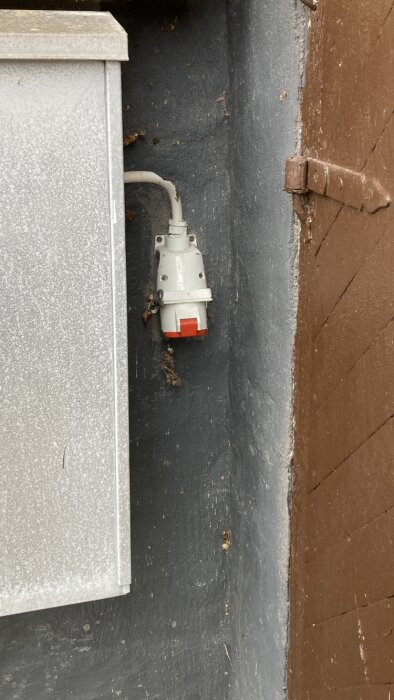 En röd och vit industriell strömuttag installerad på en vägg under en carport med en överbliven upprullad kabel.