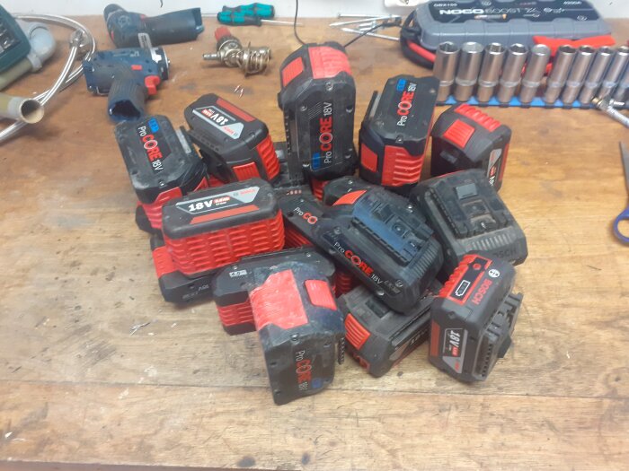 Oordnad samling av batterier för elverktyg på ett arbetsbänk.