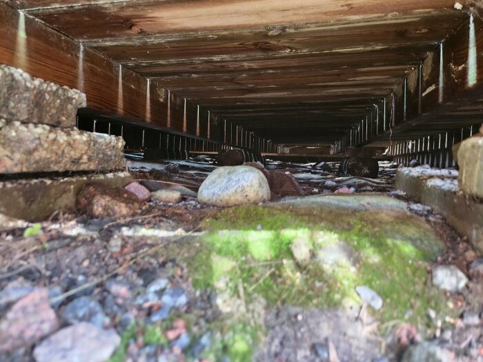 Undersida av byggstruktur vilande på stenplattor och stockar, ej nedgrävda.