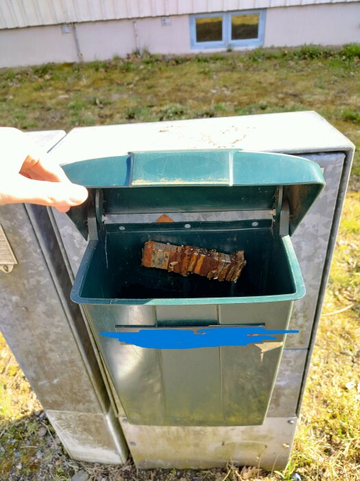 Gammal brevlåda fastsatt på ett elskåp med en sönderrostad stolpe i, locket går bara öppna en tredjedel.