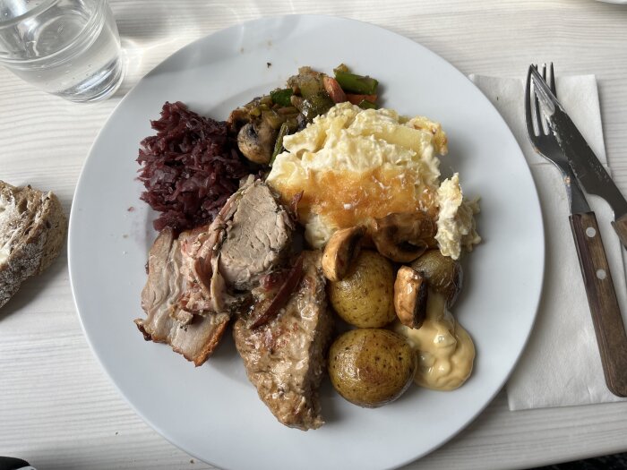 Tallrik med varmrätter inklusive lammfilé inlindad i bacon, dansk fläskstek, potatisgratäng och rödkål.