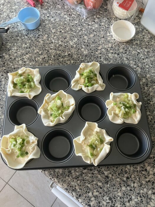 Oformade smördegsknyten med rökt lax och salladslök i en muffinsplåt, redo att gräddas.