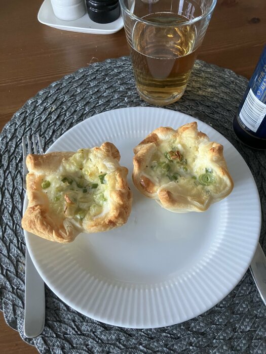 Smördegsknyten med rökt lax och salladslök serverade på en vit tallrik med ett glas dryck.