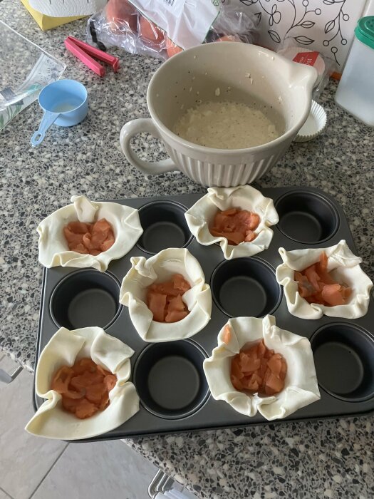 Muffinsplåt med smördegsfickor fyllda med rökt lax, redo för äggstanning och mozzarella.