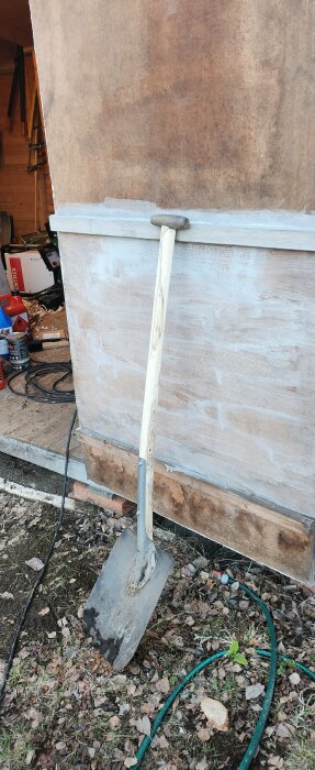 En trasig skyffel står lutad mot en vägg med ett handtillverkat trähandtag från en ek.