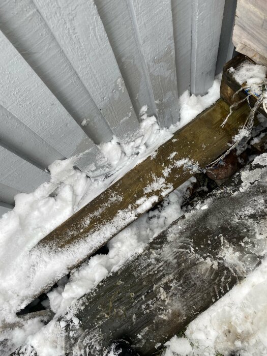 Exponerad elektrisk kabel utan skyddsrör löper längs en vägg kantad av snö, nära gräsmattan vid ett garage.