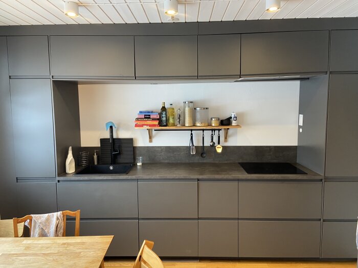 Modernt kök med mörka väggskåp, vit spontad träpanel som innertak och inbyggt spisområde.
