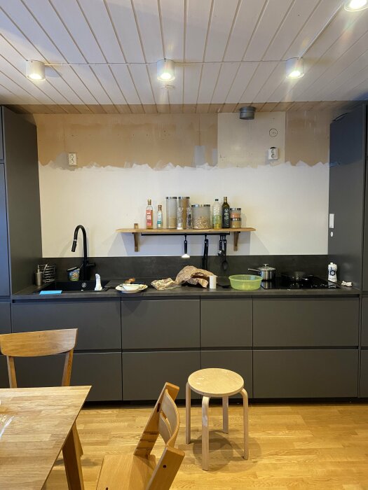 Kök med spontat träpaneltak och gråa Ikea-skåp under en oavslutad vägginstallation.