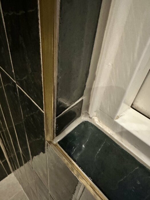Ojämna kakelplattor och slarvigt applicerad silikonfog vid hörn i ett badrum under renovering.