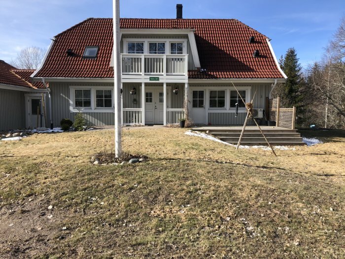 Traditionellt rött hus med vita knutar och flaggstång framför på en gräsmark redo för trädplantering.