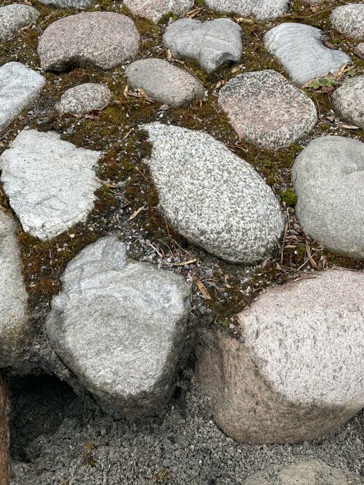 Smal stenlagd slänt med stora runda stenar, mossa och underliggande stenmjöl synligt mellan stenarna.