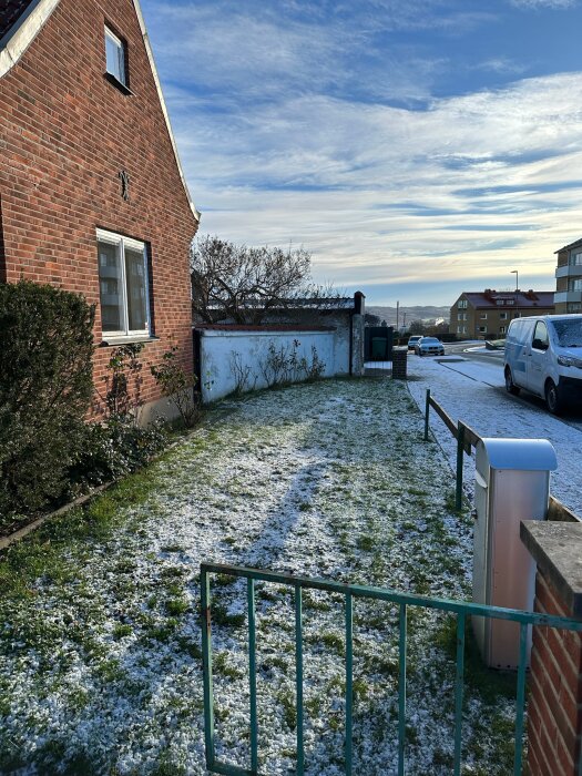 Husets framsida med snötäckt gräsmatta och lågt staket, intill en gata och andra hus i området.