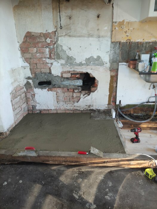 Köksrenovering med nylagt betonggolv och en delvis bilad murstock som visar skador och hål.