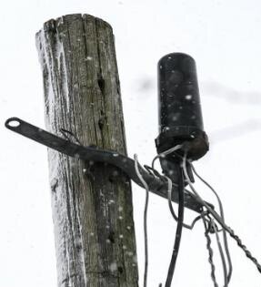 Skarv-/förgreningsbox för telefonkabel fäst på en trästolpe med en svart strumpa över kablar som skydd under snöfall.