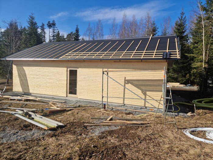 Nybyggt hus med omonterad liggande panel och pågående takarbete under solig himmel.