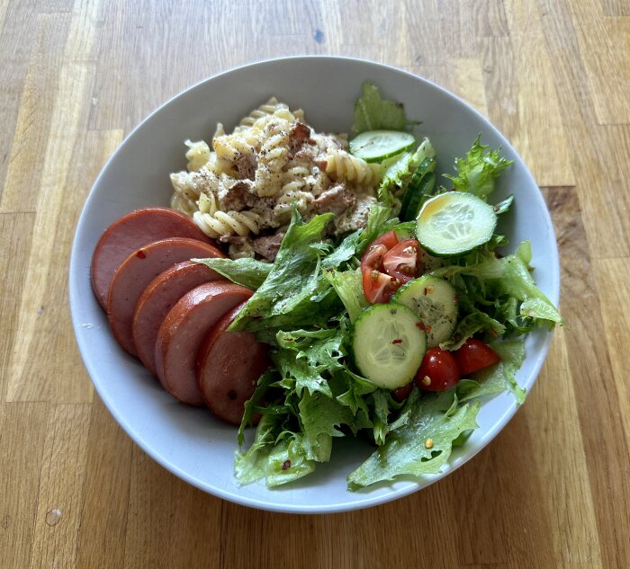 Tallrik med pastagratäng, skivor av jokkmokkskorv och grönsallad med gurka och tomat.
