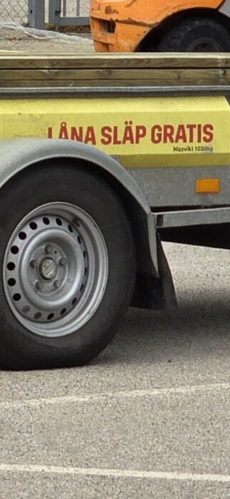 Del av släpvagn med hjul och texten "I LÅNA SLÄP GRATIS", lämm synlig ovanför regskyltsflärp.