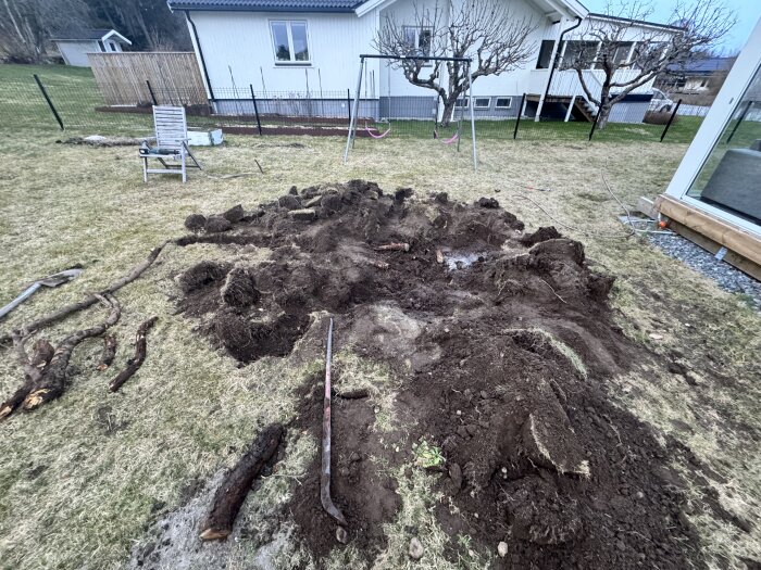 Grävd trädgård med uppochnervända jordhögar, en spade och uppgrävda rötter framför ett bostadshus.