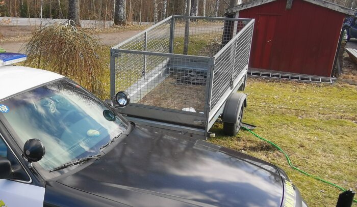 Obromsad släpvagn med nätgrindar parkerad på en gräsmatta bredvid en personbil.