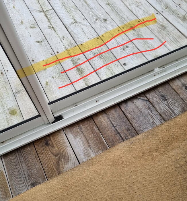 Trädäck med måttmarkerat gult streck och röda linjer vid glasparti för byggprojekt.