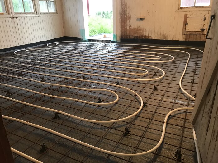 Installation av golvvärme med vit rör slinga på armeringsjärn före gjutning i ett rum under renovering.