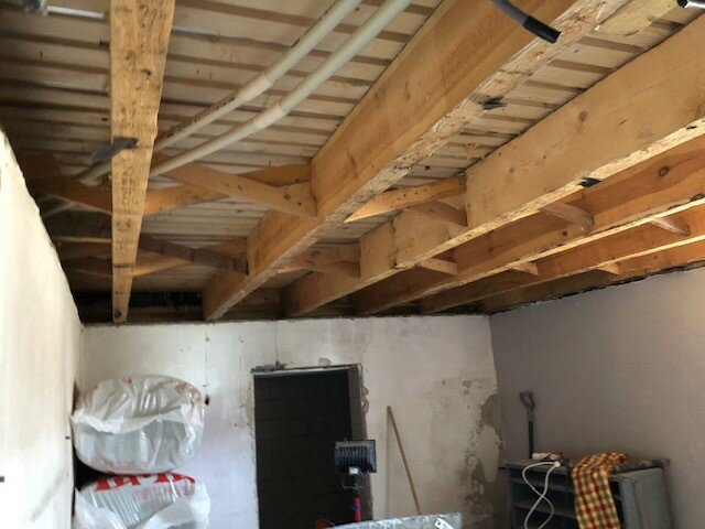 Orenoverad källare med synliga träbjälkar i taket och isoleringsmaterial längs väggen, före ombyggnad.