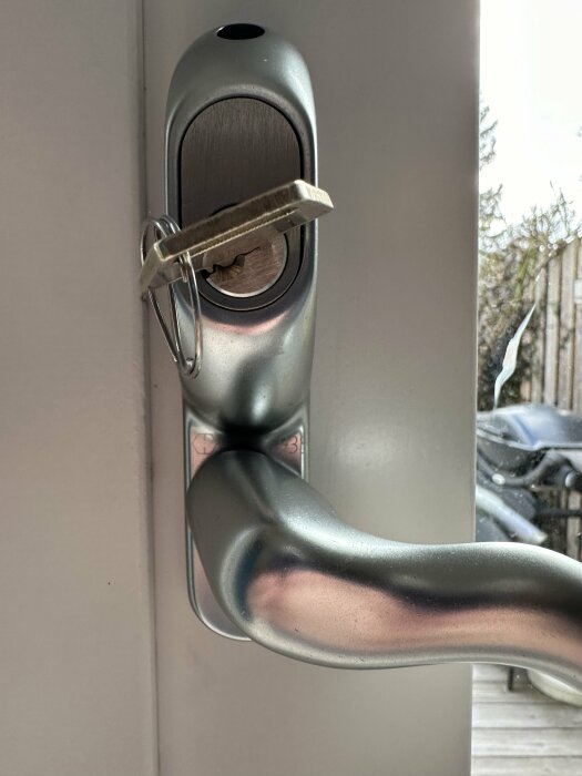 Altandörr med silverfärgat Hoppe Tokyo 93S handtag och nyckel i låset, sett inifrån.