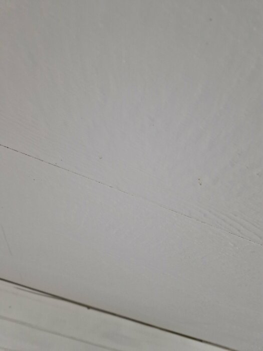 Brunaktiga fläckar och prickar på ett vitt tak, möjligt fuktskador nära taklampa.